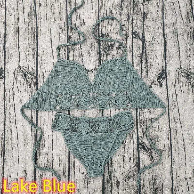 A two-piece dusty blue crocheted swimwear set, featuring a triangle top and matching low-rise bottoms, laid out flat against a weathered gray wood plank backdrop with a 'Lake Blue' color label text