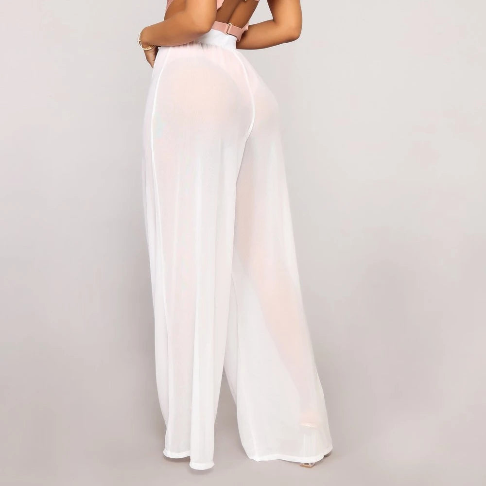 Model from the side-back wearing Echo & Air women's Sheer Wide Leg Pants in white, showcasing the loose bohemian silhouette and see-through mesh fabric.
