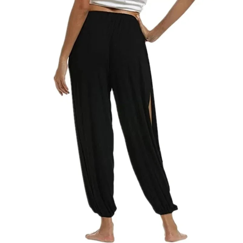 Model from the side-back wearing Echo & Air women's Ethereal Side-Slit Lounge Pants in black showcasing the high leg slit and loose harem fit.